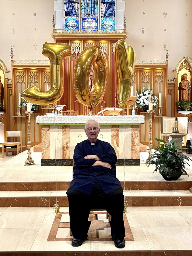 Fr. Kelly, with balloons that read “joy” behind him